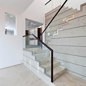Treppenaufgang mit Verkleidung in imi-beton PLUS Glattschalung grau und Glasgeländer mit schwarzer Griffleiste
