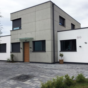 Hausfassade aus der Einfahrt mit Hauptgebäude mit imi-Fassade aus Glattschalung grau und Seitengebäude in weiß