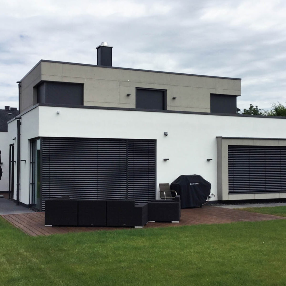 Hausfassade vom Garten aus mit weißem Erdgeschoss und erstem Stock mit einer imi Fassade in Glattschalung grau